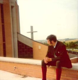 Bruder Sepp Schwaller sitzt als junger Mann auf einer Kirchenmauer.